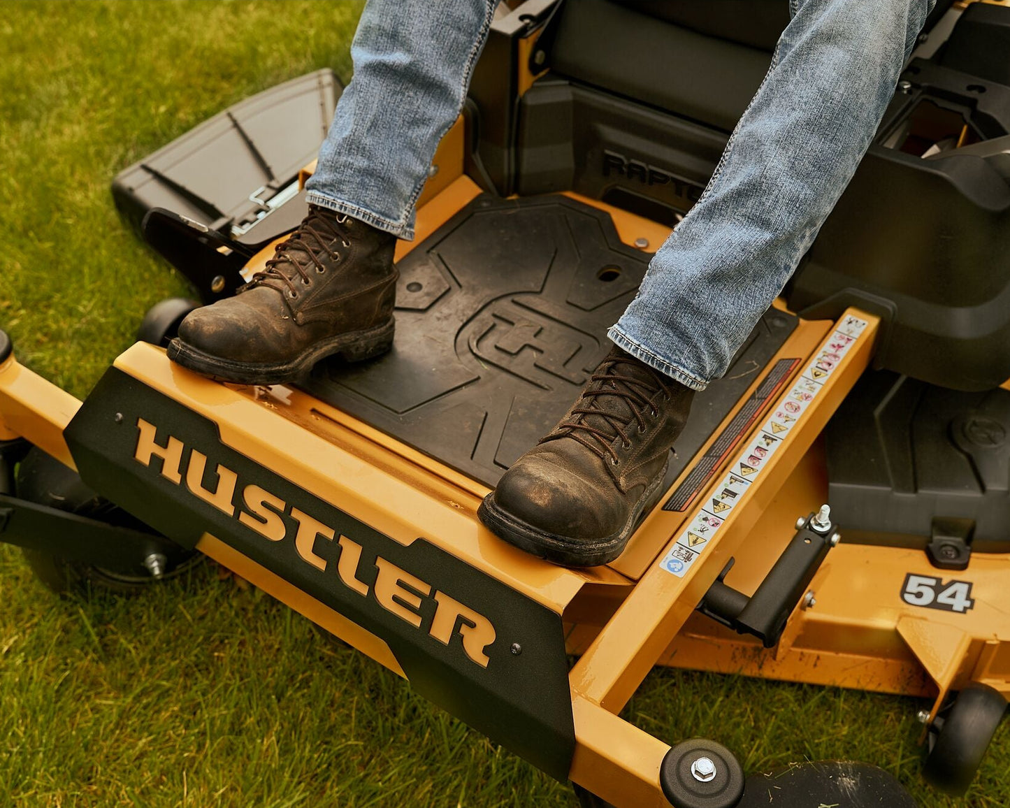Person operating a Hustler lawn mower on grass