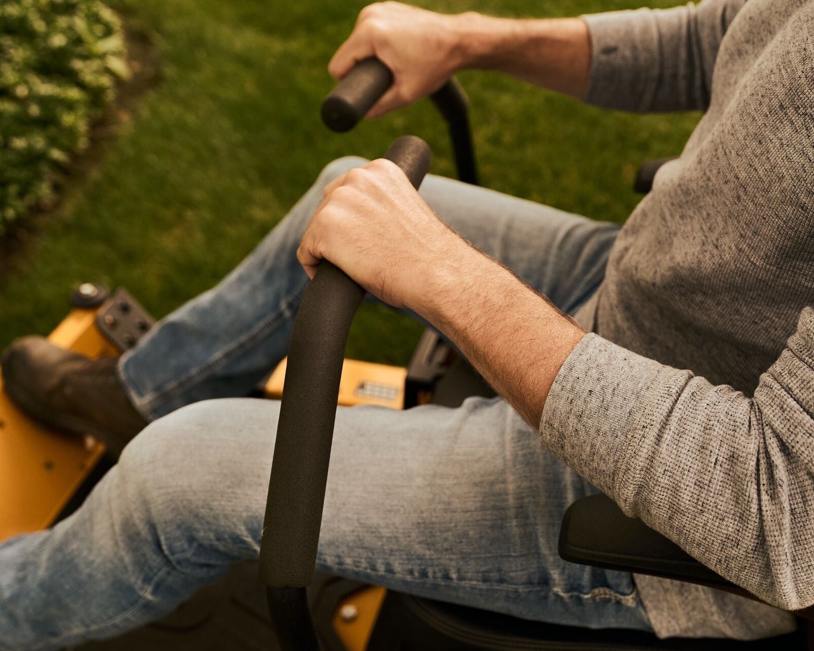 Person using a lawn mower with a focus on their hands and legs.