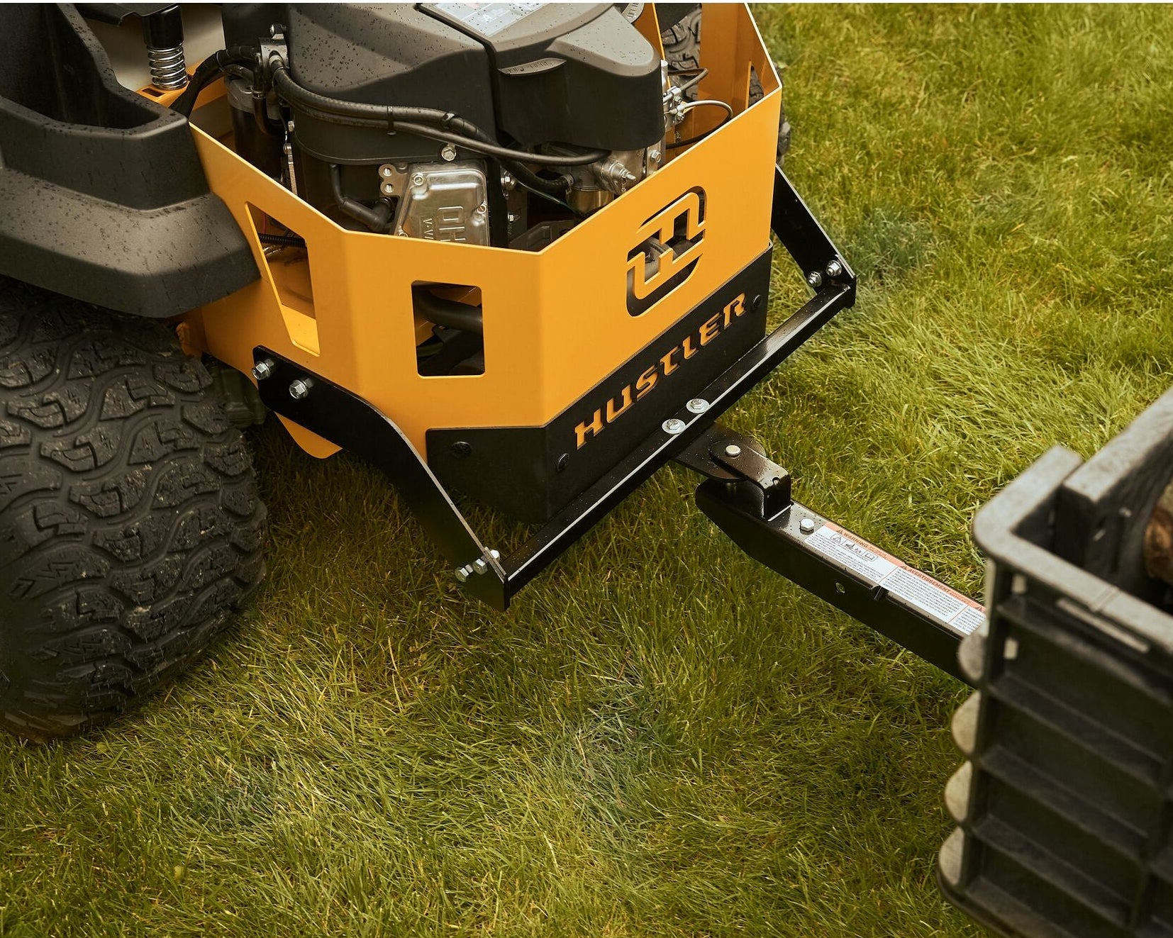 Close-up of a Hustler lawn mower on grass with a trailer attached.