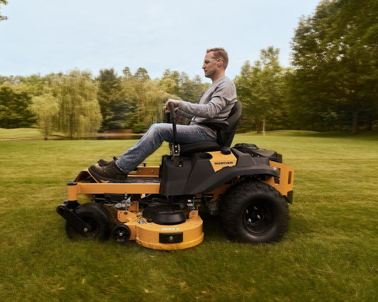 Man operating a yellow riding lawn mower in a grassy field with trees in the background