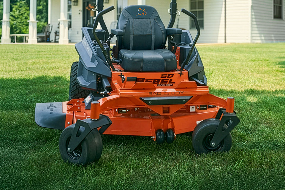 Orange zero-turn lawn mower on a grassy lawn with a house in the background