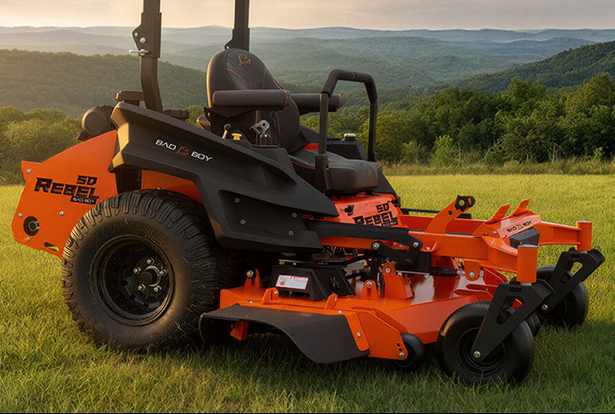 Orange riding lawn mower on a grassy field with mountains in the background